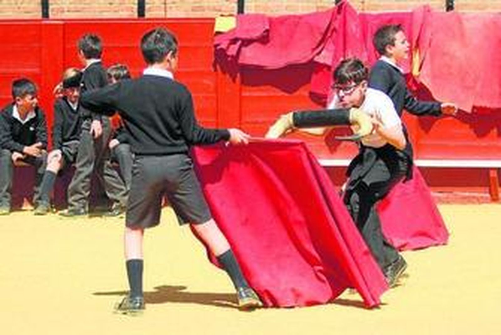 Dos escolares, en primer plano, juegan al toro en la Maestranza.