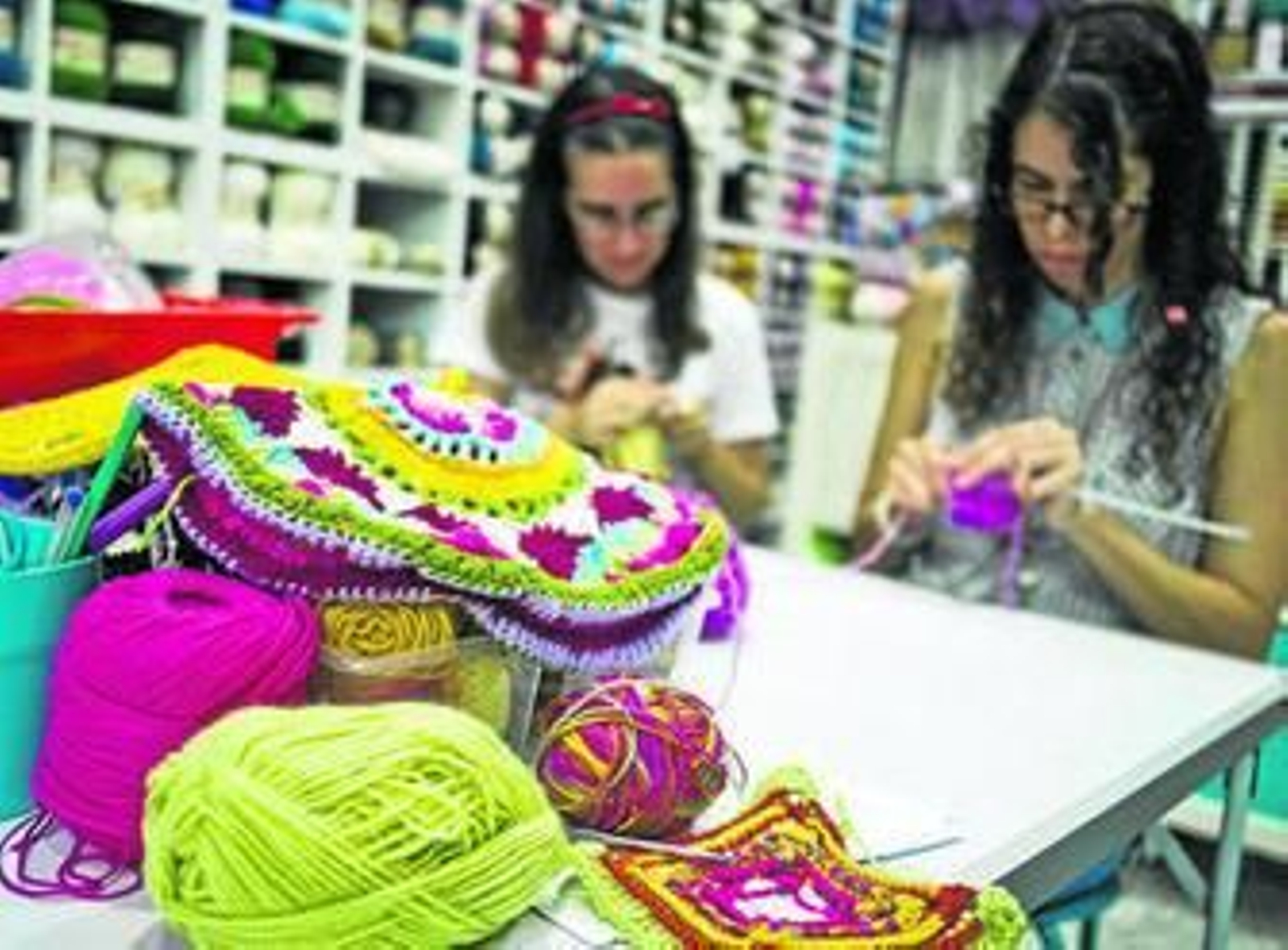 Dos voluntarias onubenses tejen varias prendas.