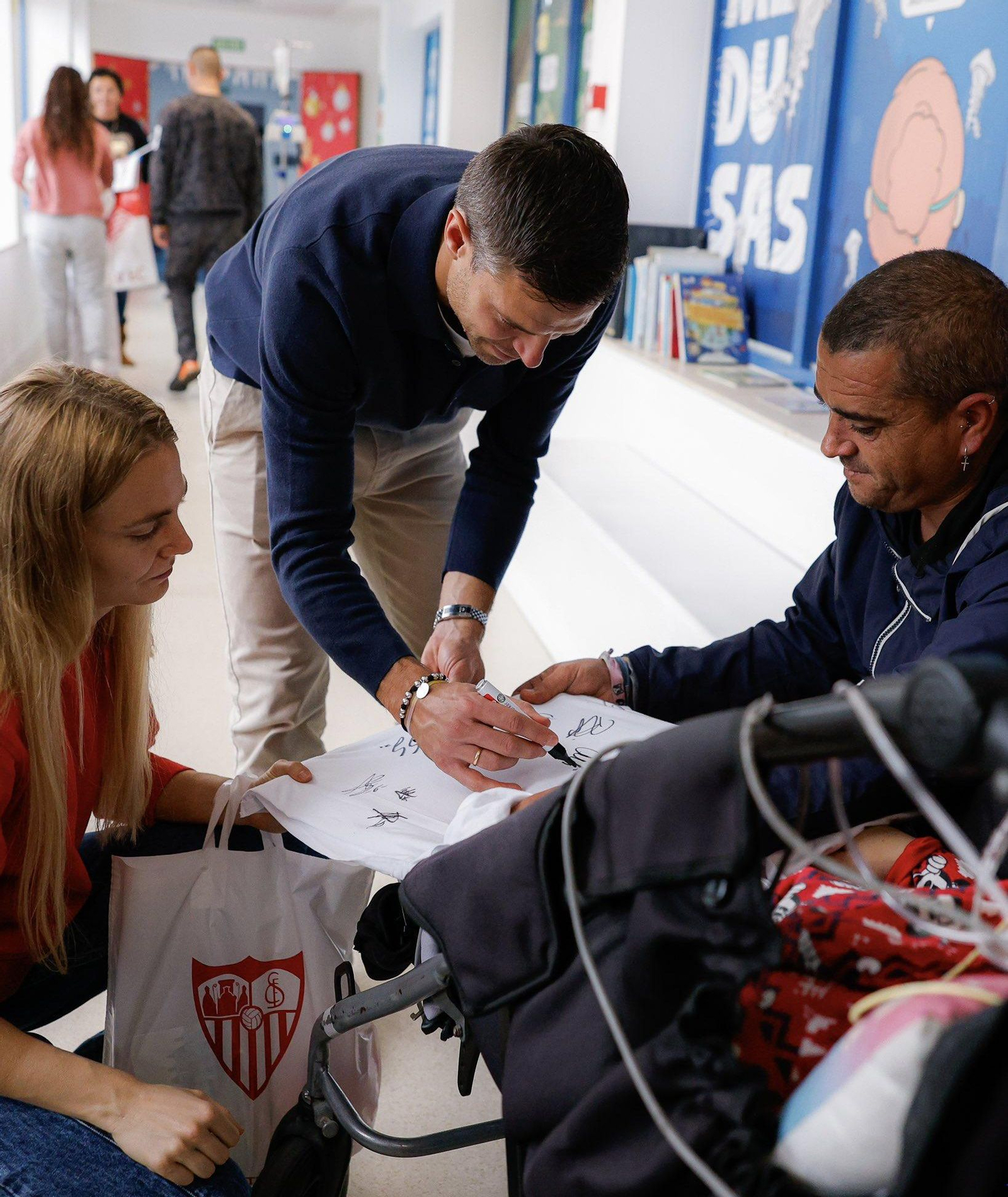 Azpilicueta echa un autógrafo a una zamarra blanca a un niño ingresado junto a sus familiares.