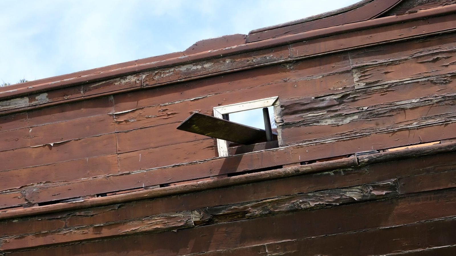 Un tablón asoma por uno de los ventanucos de la Faluca, cuya madera agrietada implora tratamientos de urgencia antes de que el barco, que costó solo su construcción 180.000 euros, sea del todo insalvable.