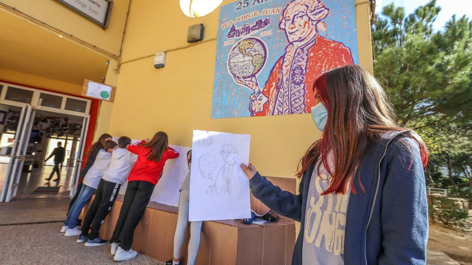 Alumnos pintan la figura de Jorge Juan siguiendo el cartel de la puerta del instituto.