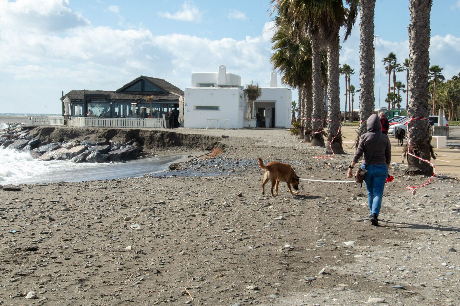 Unas personas pasean junto al Hoyo 19 con la arena cada vez más cerca de la Senda Litoral