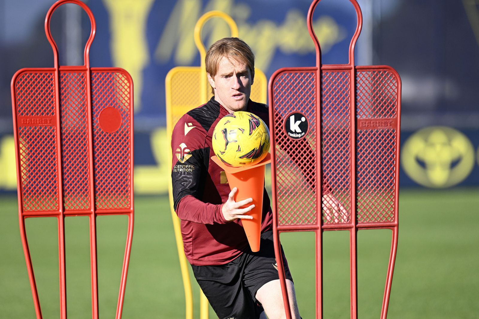 Gesto de concentración de Álex mientras sostiene un balón con un cono durante un ejercicio.