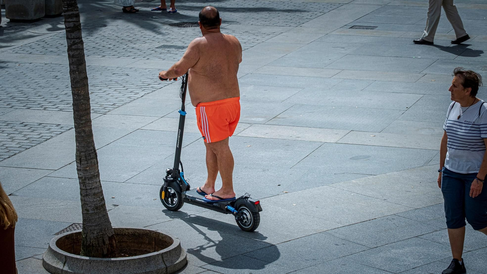 Un hombre en bañador circula con patinete en Cádiz.