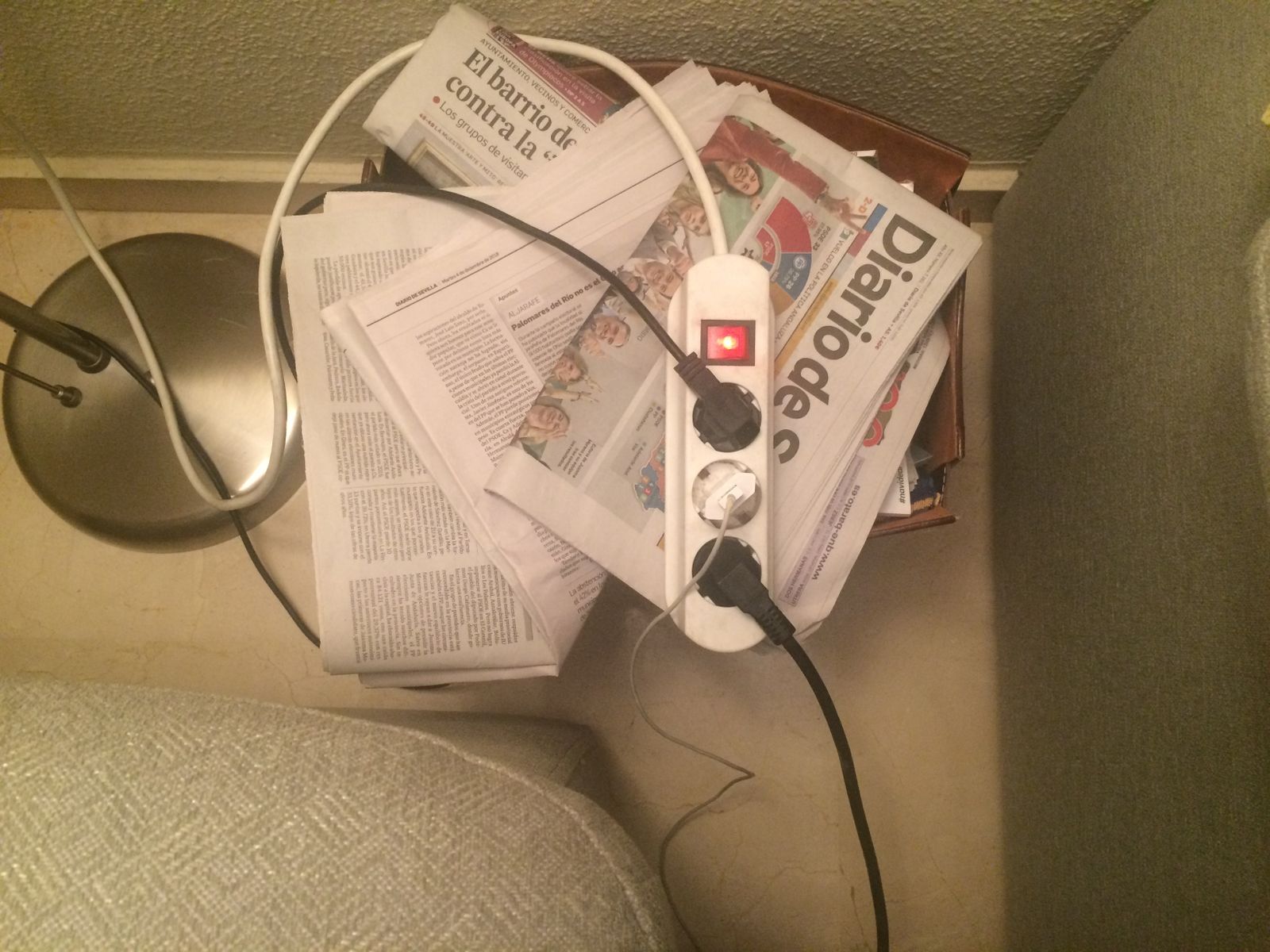 Una regleta con varios aparatos enchufados y colocada sobre un revistero.