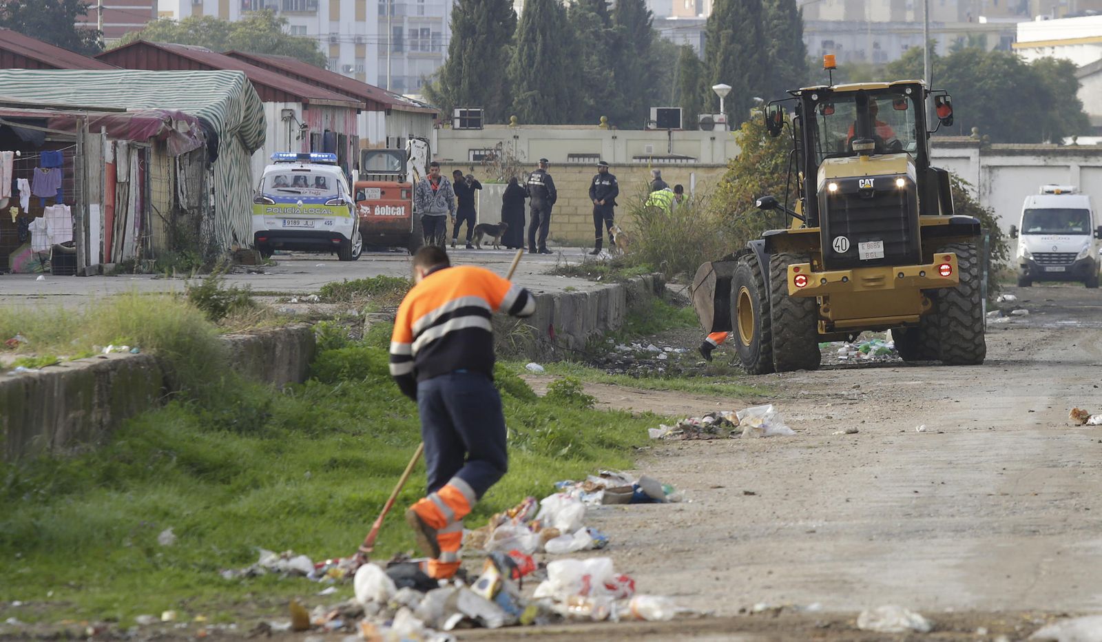 Limpieza de residuos, con la Policía Local al fondo, el pasado martes en la parte del asentamiento más próxima a la tapia del cementerio.