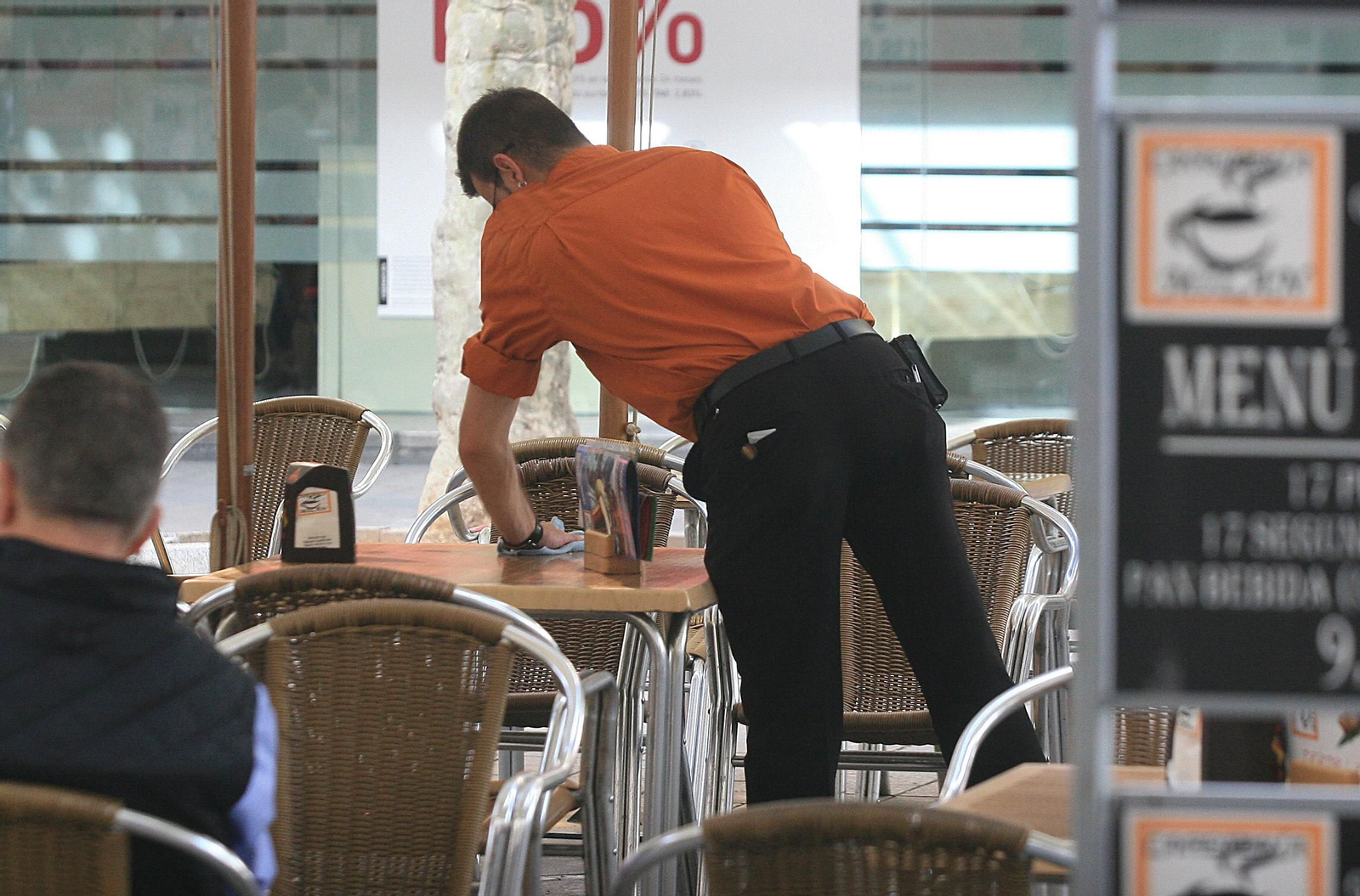 Un camarero limpia una mesa durante su turno de trabajo. Un camarero limpia una mesa durante su turno de trabajo.