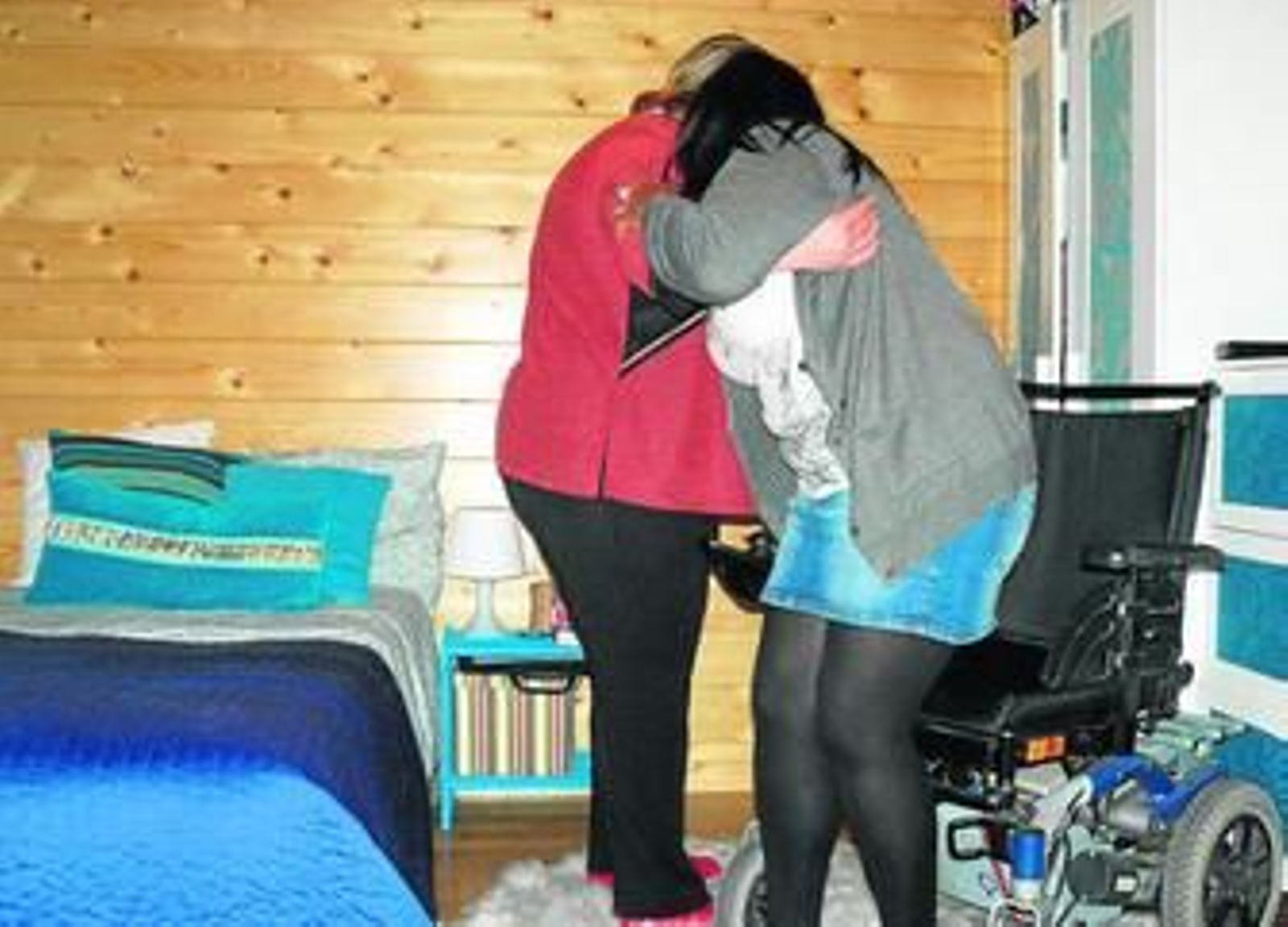 Una asistenta ayuda a sentarse en una silla de ruedas a una persona dependiente.