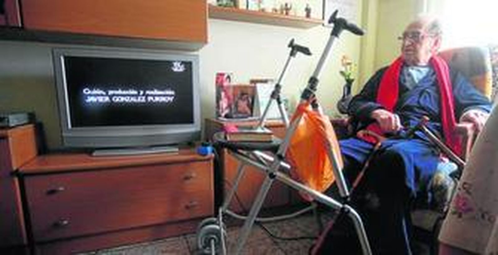 Francisco Trujillo ve la televisión en su casa junto a su andador y sus bastones.