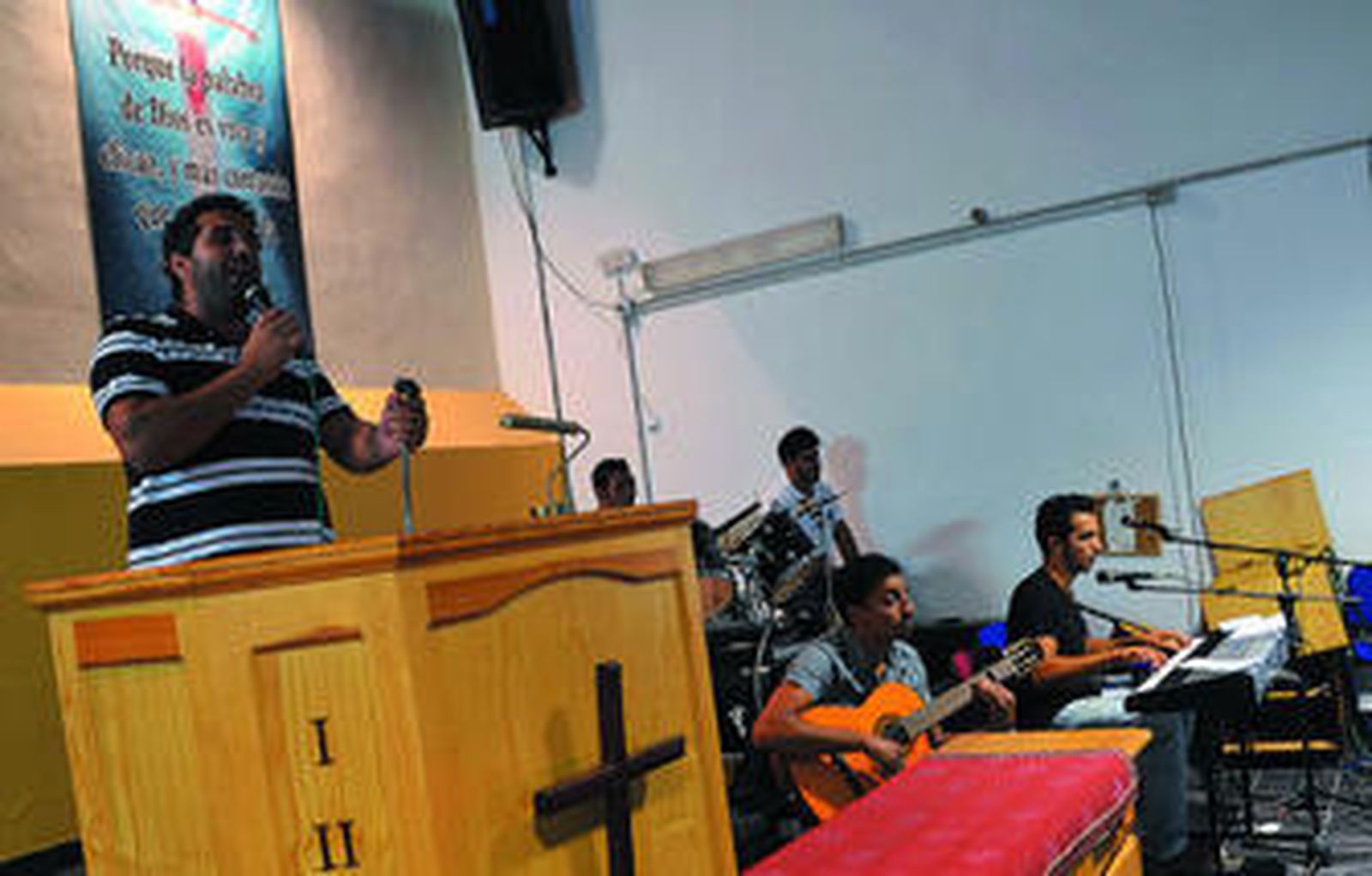 Un joven, micrófono en mano, inicia el culto el pasado jueves en la nave que la Iglesia Evangélica Filadelfia tiene alquilada en Cuatro Caminos. Al fondo, los músicos.