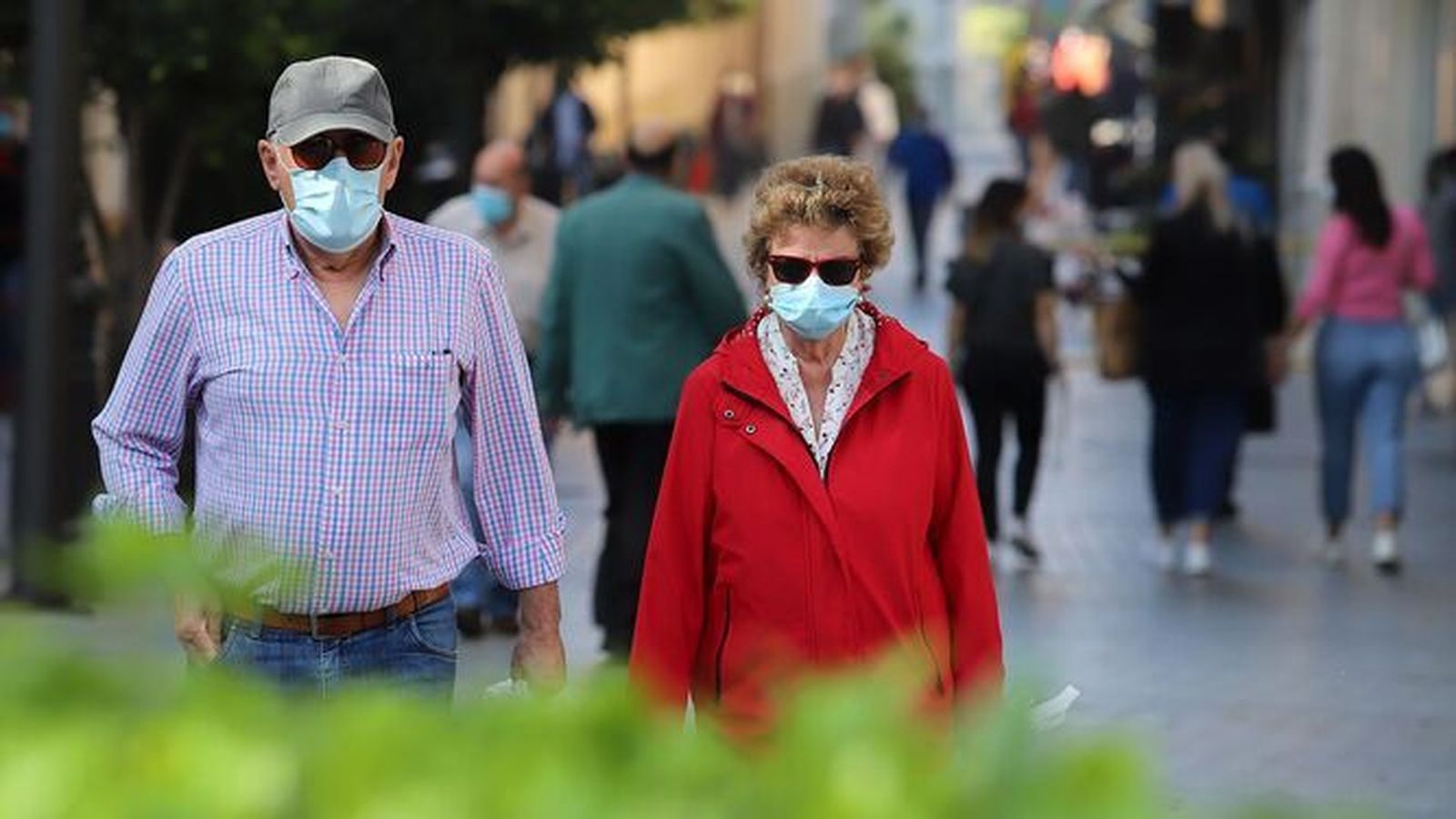 Dos personas pasean, entre otras tantas, con mascarilla.