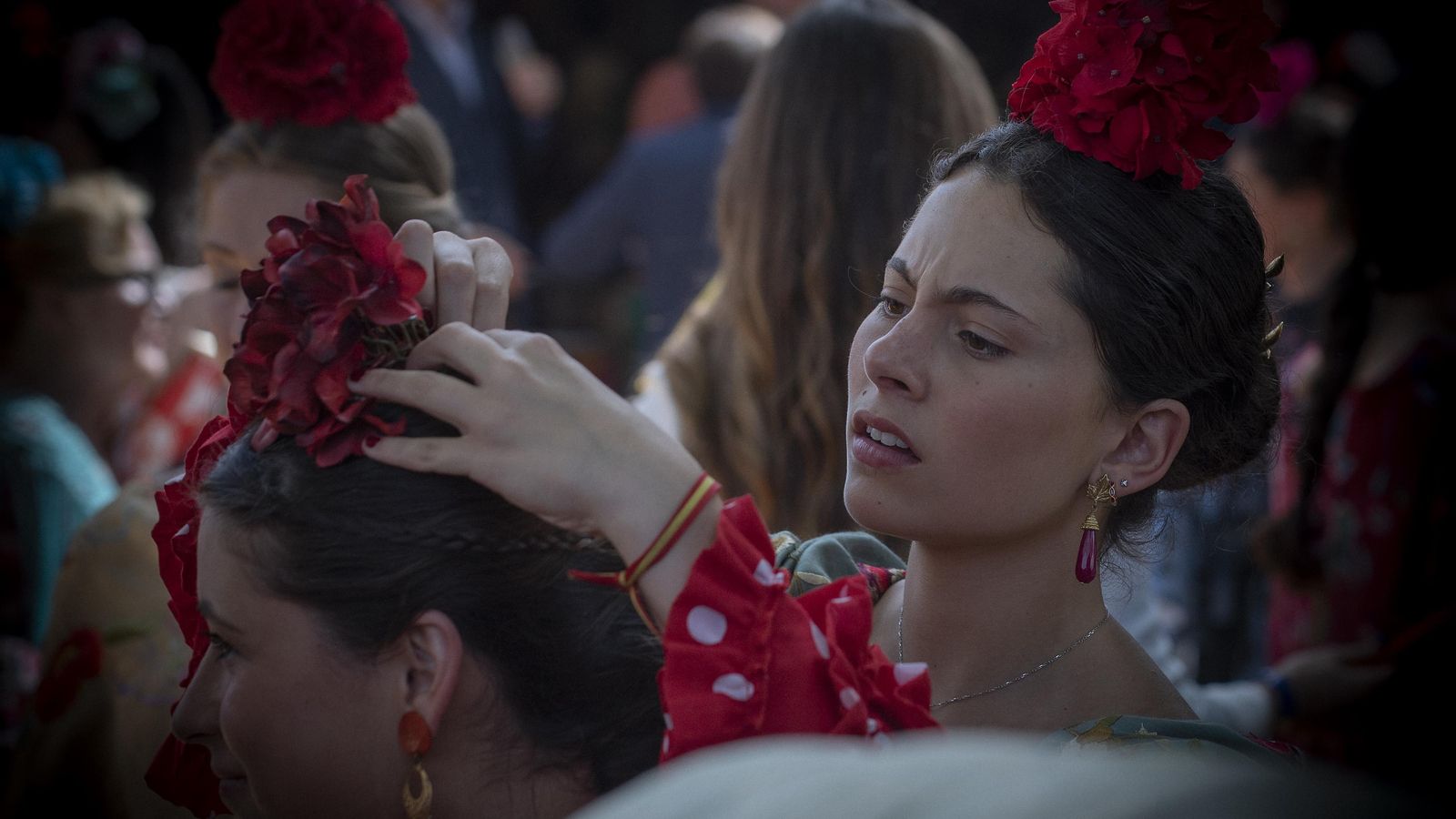 Una mujer vestida de flamenca coloca a otra la flor en la cabeza.