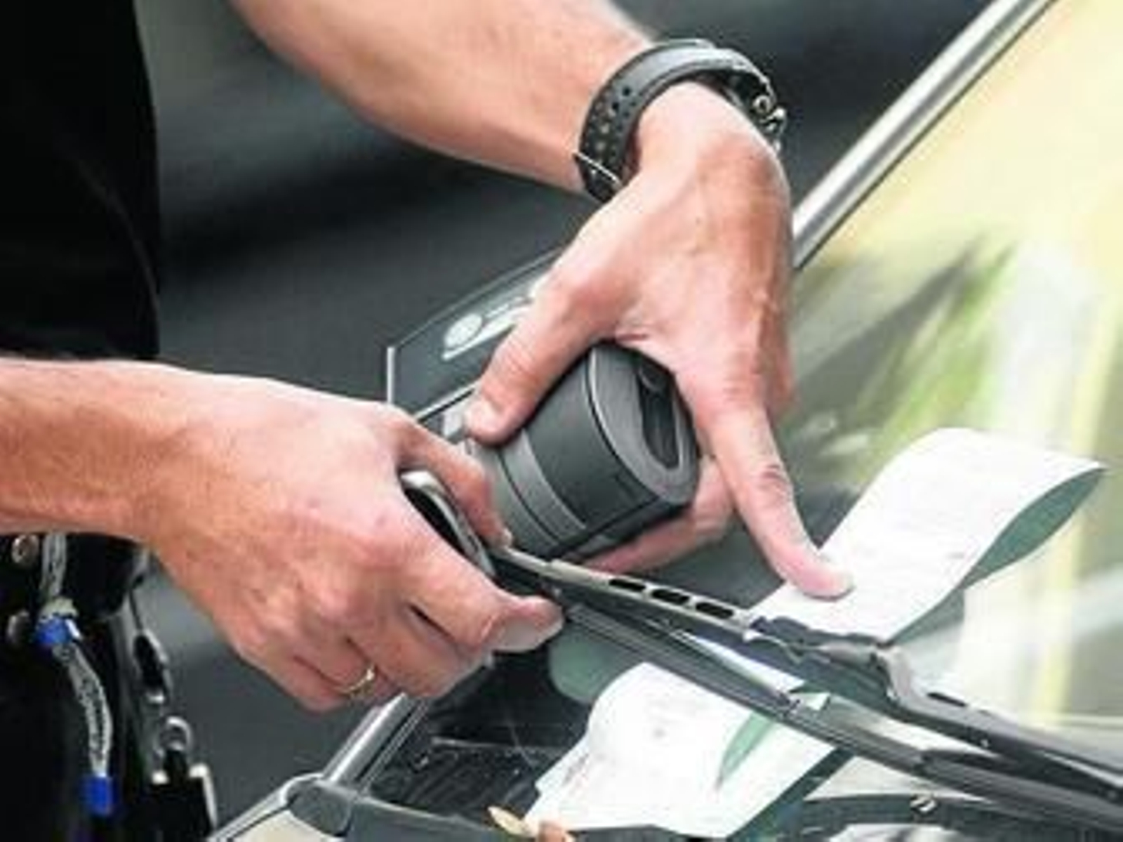 Un policía deja una multa en el parabrisas de un coche.