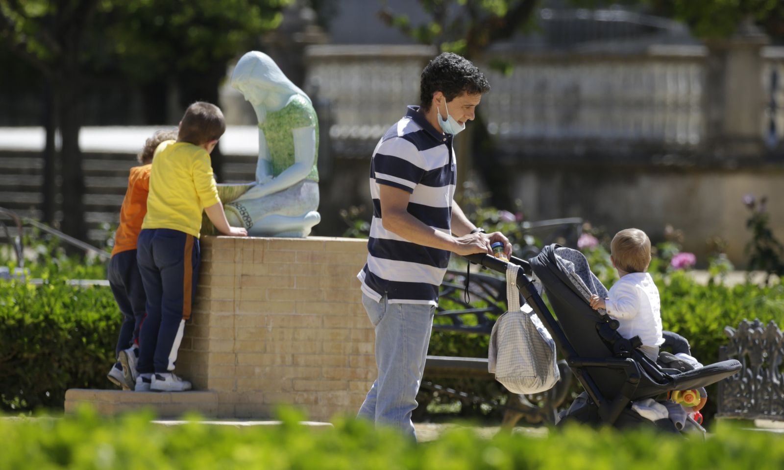 Un padre pasea a su bebé con otros dos menores al fondo.