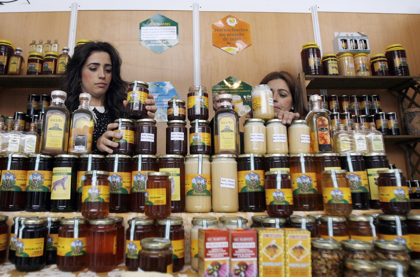 Dos mujeres colocan botes de miel en un expositor durante una edición de la feria Expomiel.