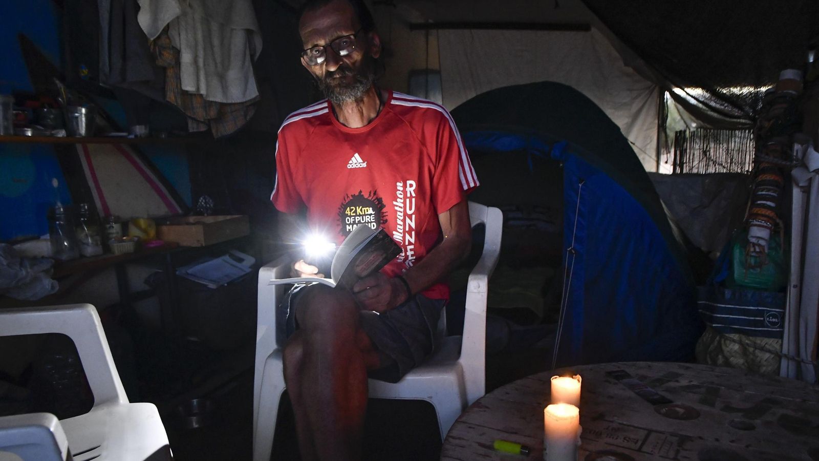 Miguel intenta leer con la linterna de su móvil y dos velas.