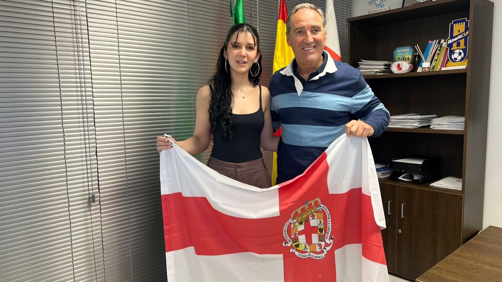 Antonio Casimiro entrega una bandera de Almería a Inés Ortega para que la exhiba en sus próximos éxitos.