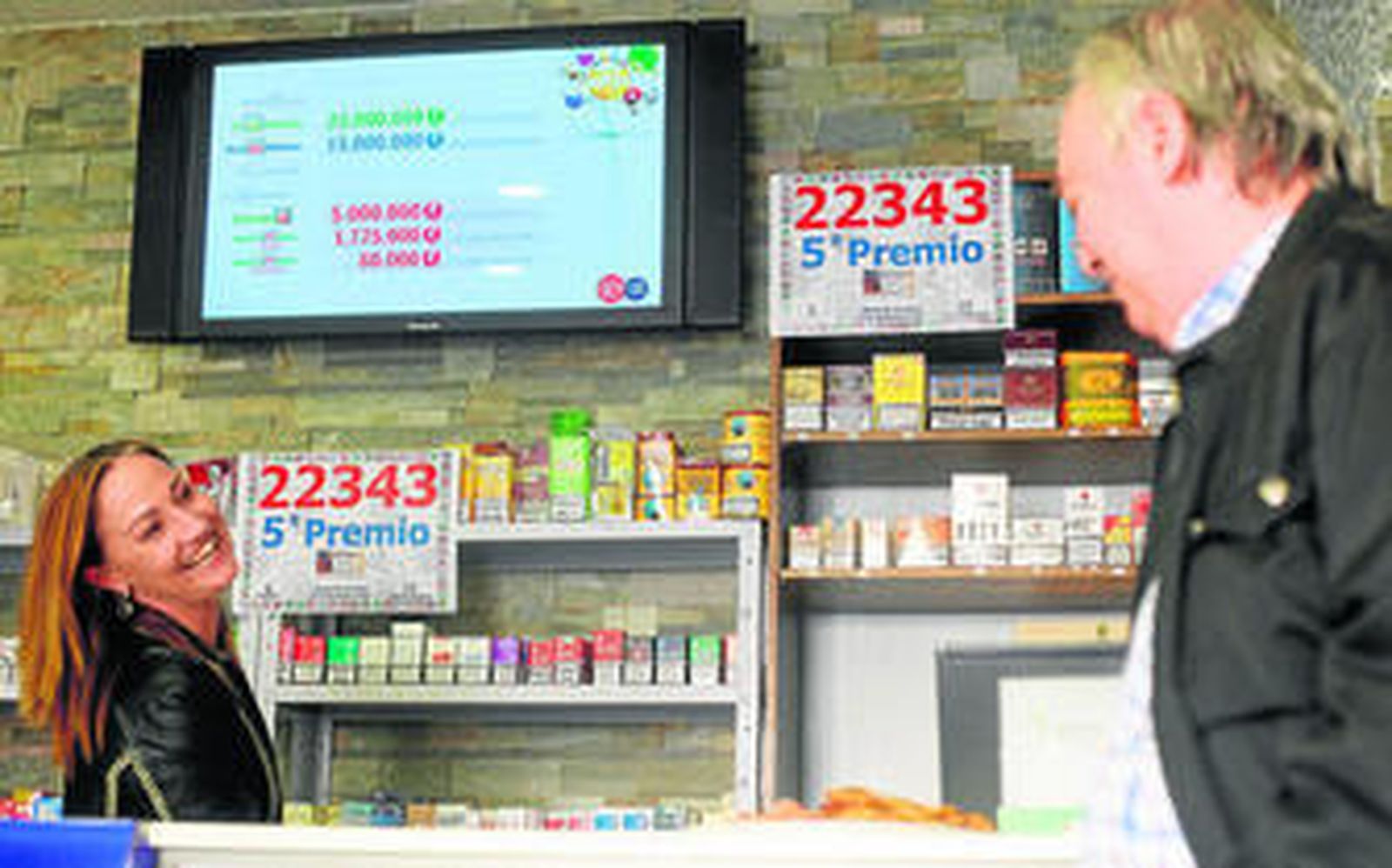 Yolanda Muñoz Celis colocando un cartel con el número premiado en presencia de un cliente del estanco.