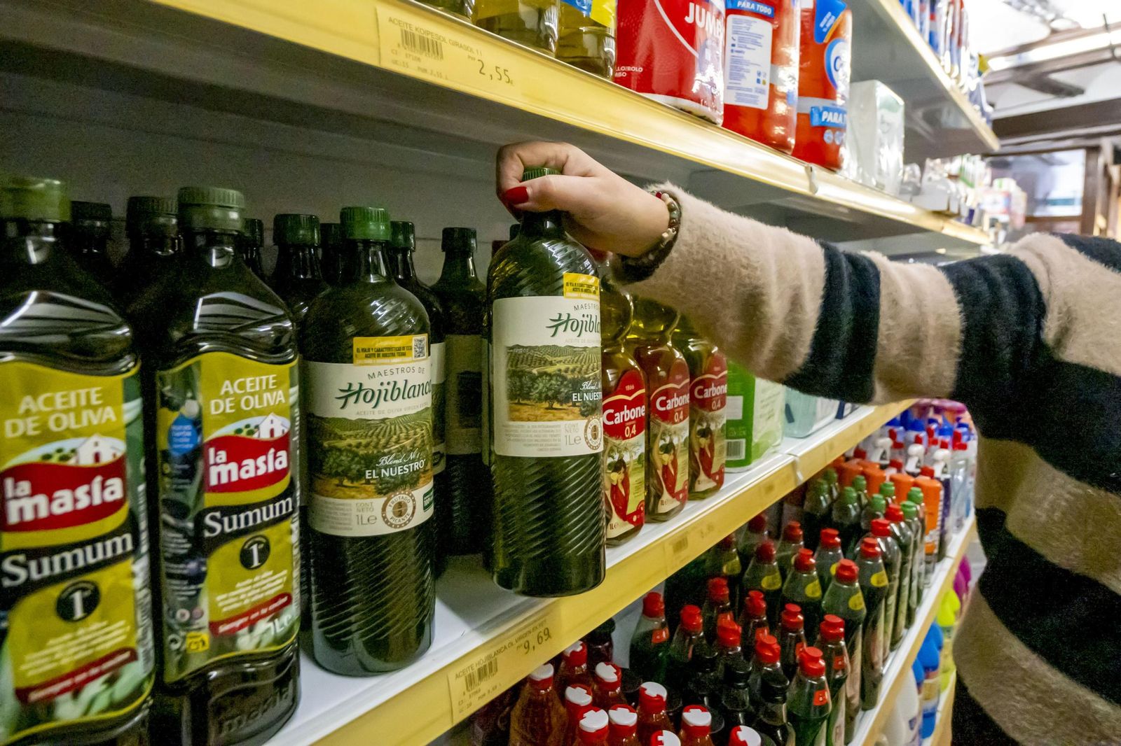 Una mujer toma una botella de aceite de oliva en un supermercado.
