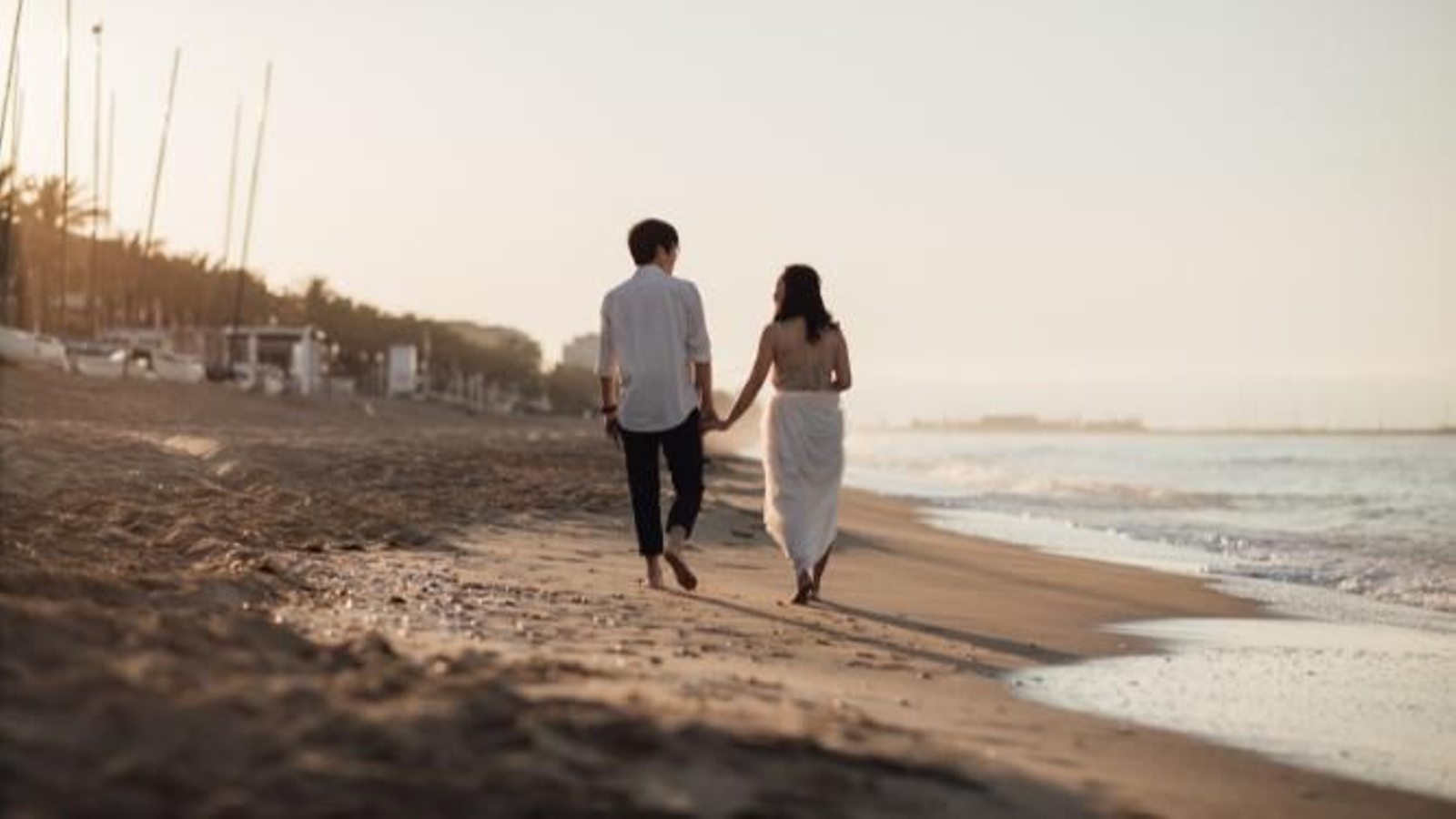 Pareja andando sin zapatos por la arena de la playa.