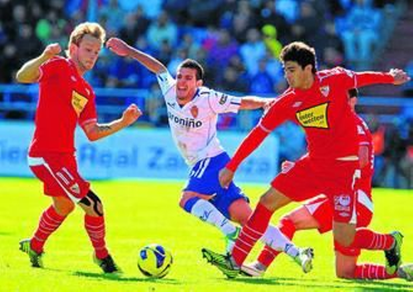 Rakitic y Perotti tratan de hacerse con el balón ante Víctor, derribado por otro jugador del Sevilla.