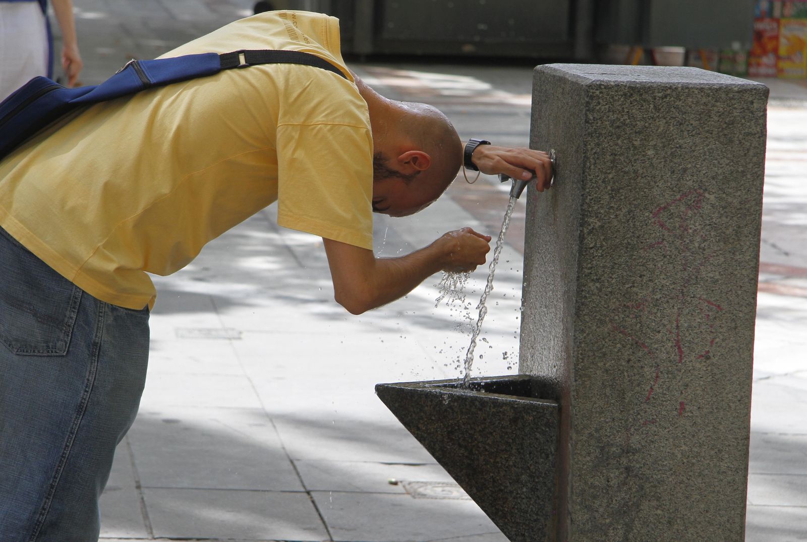 Un hombre se refresca la cabeza en una fuente