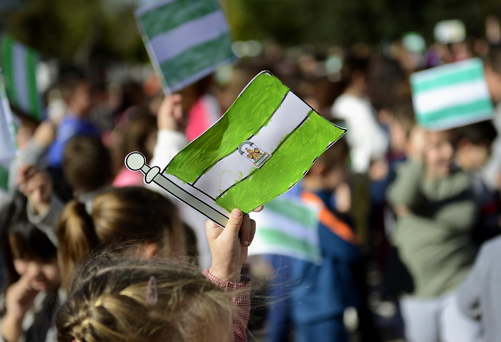 Una niña sostiene una bandera verde y blanca por el Día de Andalucía.