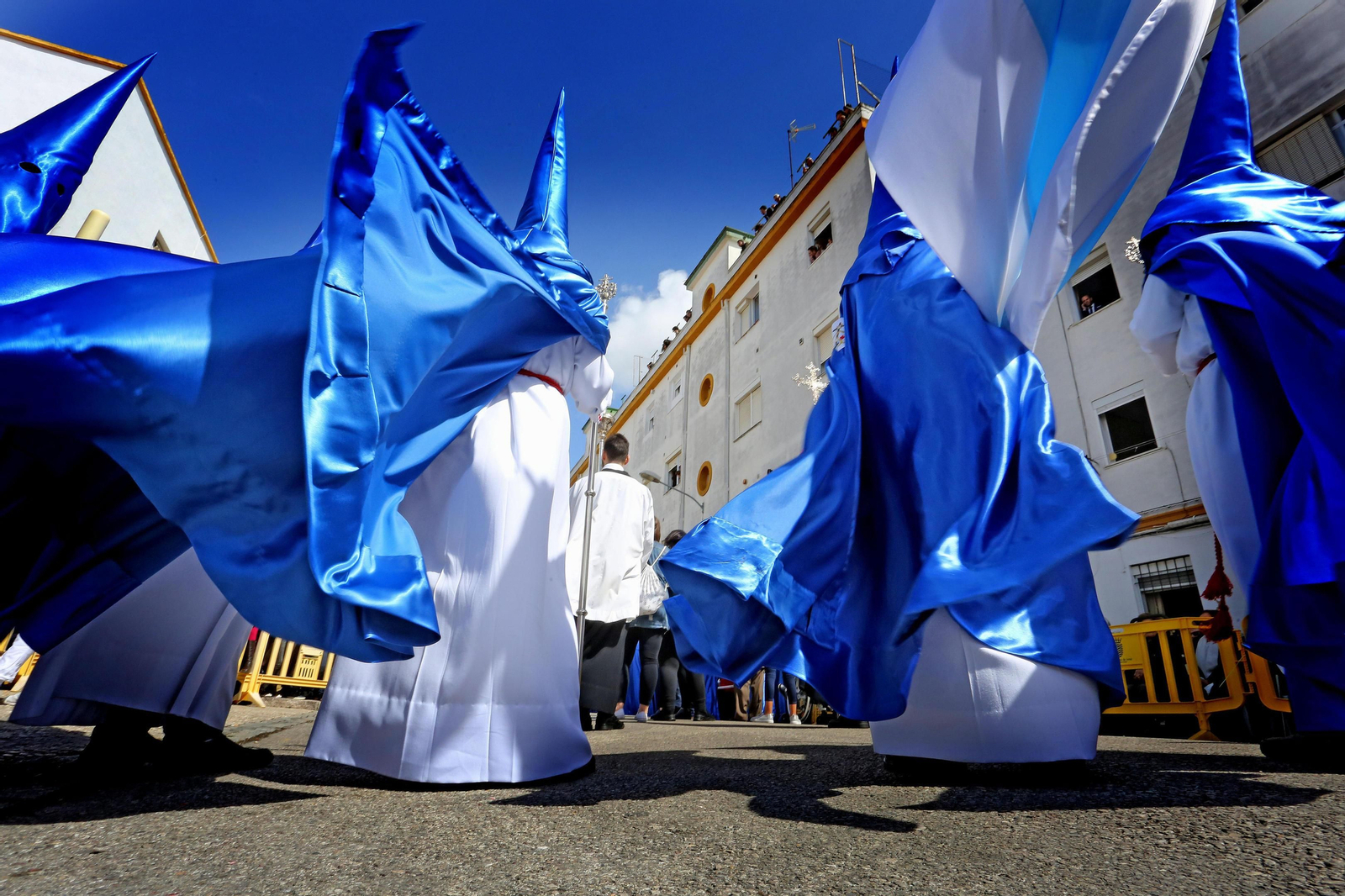 Hermanos de la Exaltación avanzan por la barriada de La Vid mientras el viento azota sus túnicas.