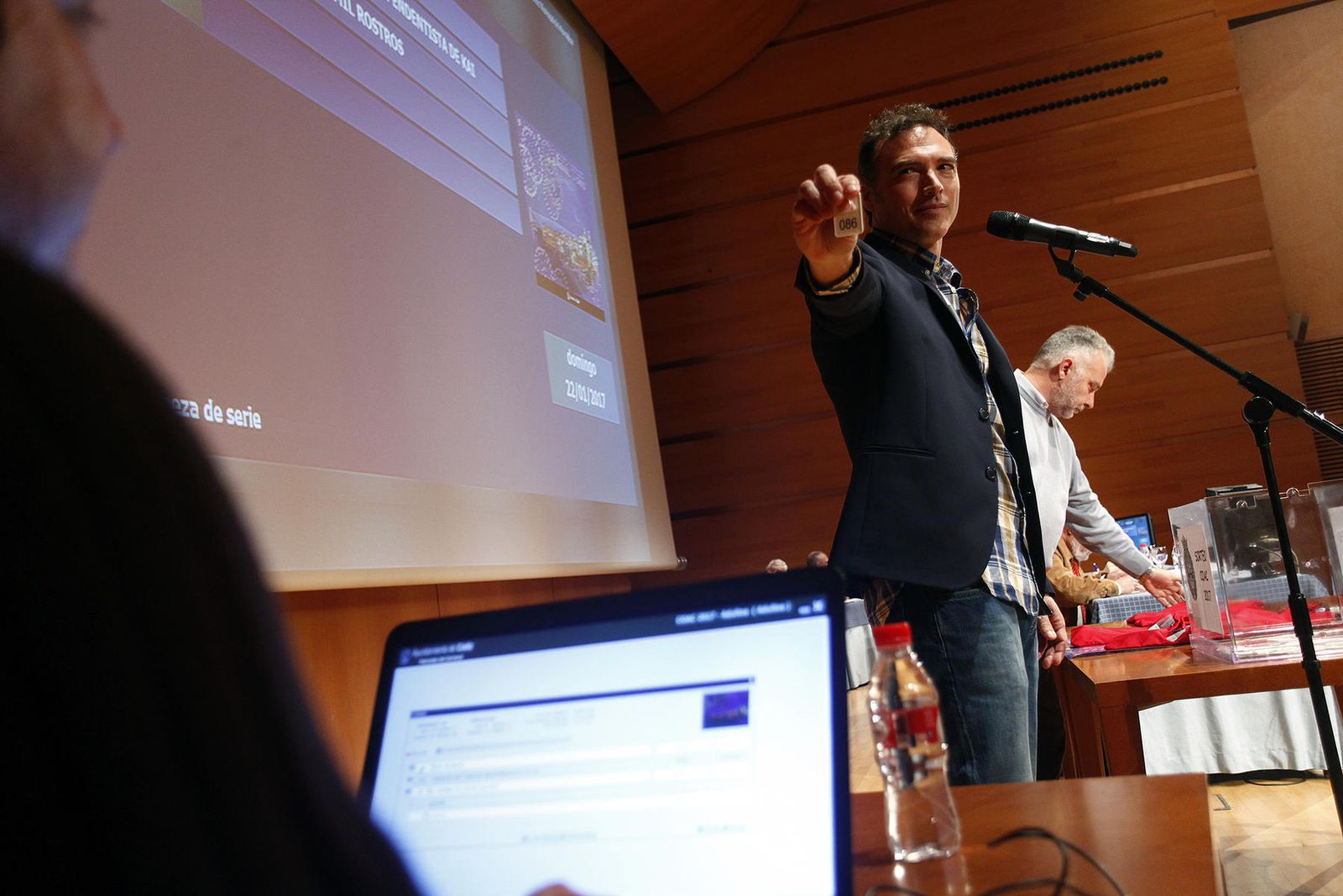 Enrique Miranda muestra al informático una de las fichas con el número adjudicado a una de las agrupaciones.