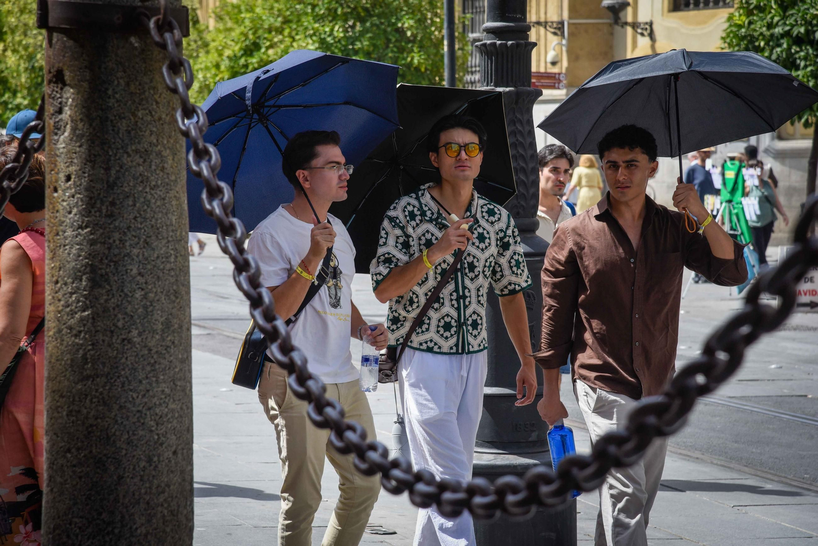 Tres turistas se protegen del sol con paraguas en Sevilla.