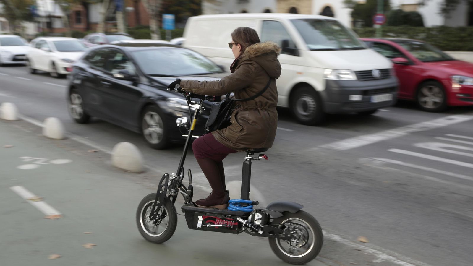 Una usuaria de patinete eléctrico con sillín se dispone a circular por el carril bici.