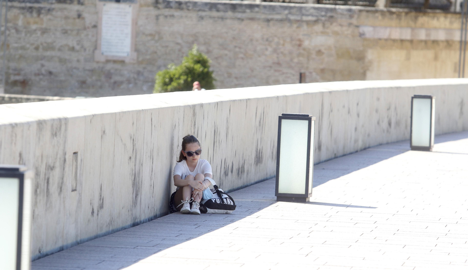 Una joven se protege del sol en la escasa sombra del muro del Puente Romano.