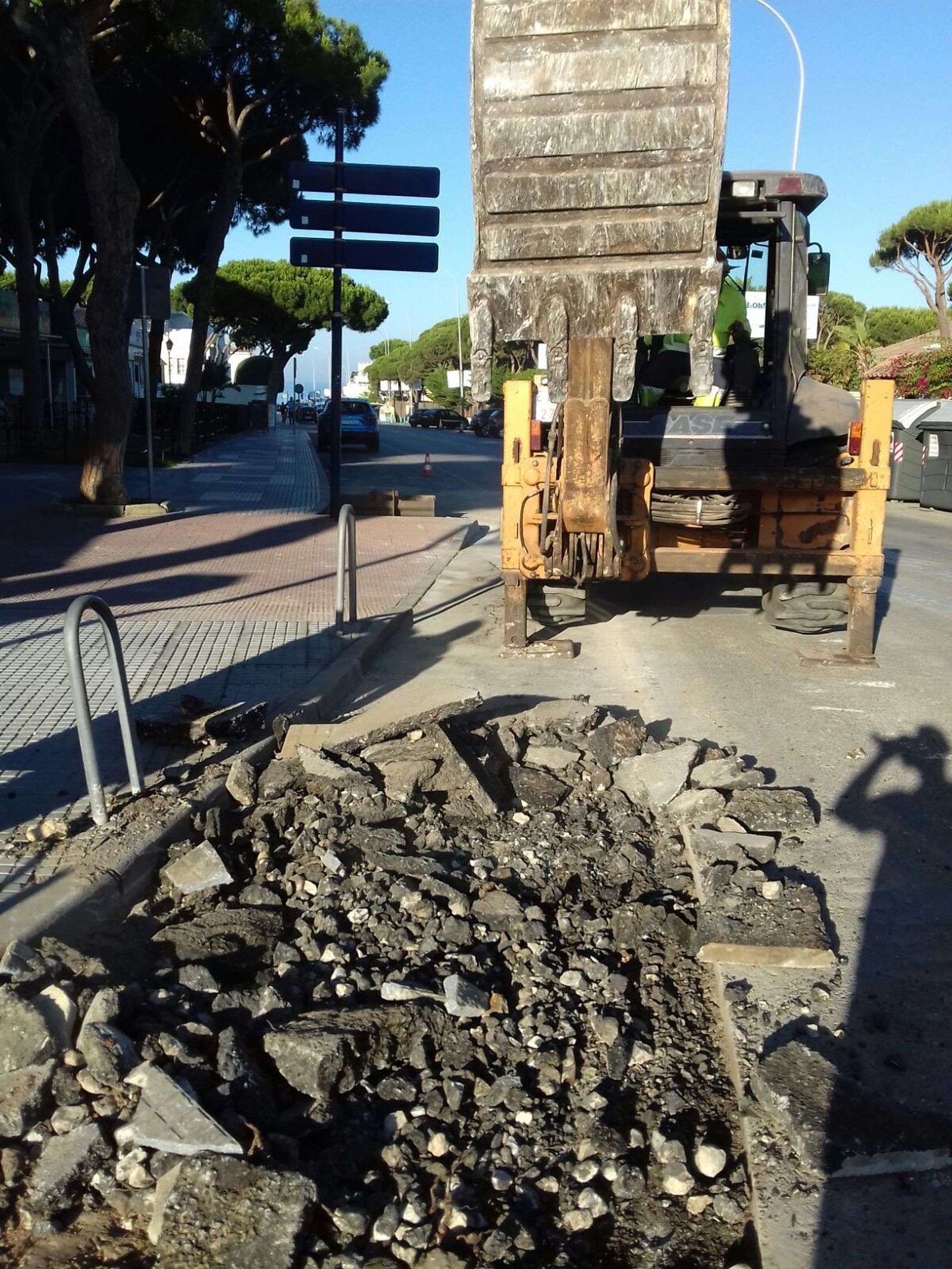 Una pala mecánica levanta el asfalto deteriorado a causa de los árboles.