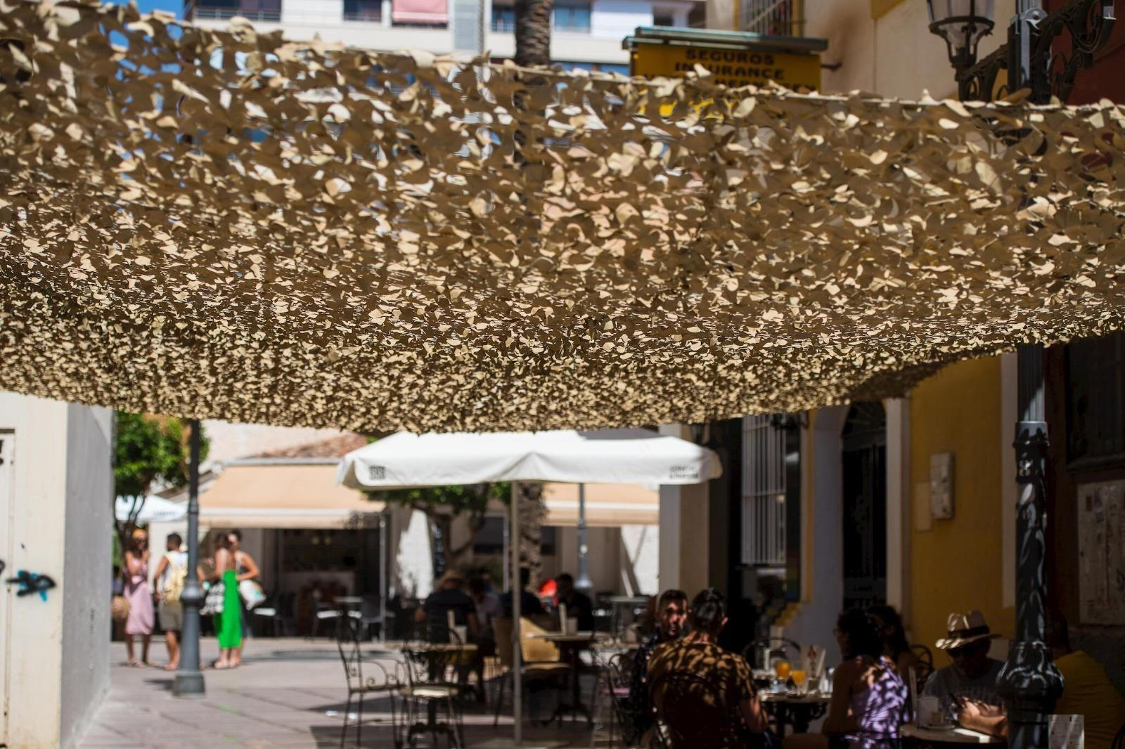 Varias personas se resguardan a la sombra de un toldo en un establecimiento de hostelería.