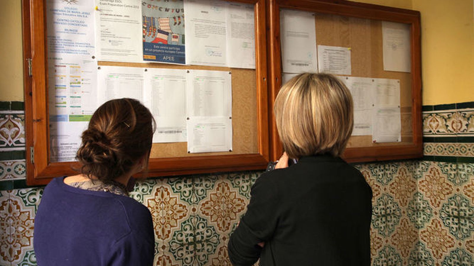 Dos mujeres observan la lista de alumnos admitidos en un colegio.