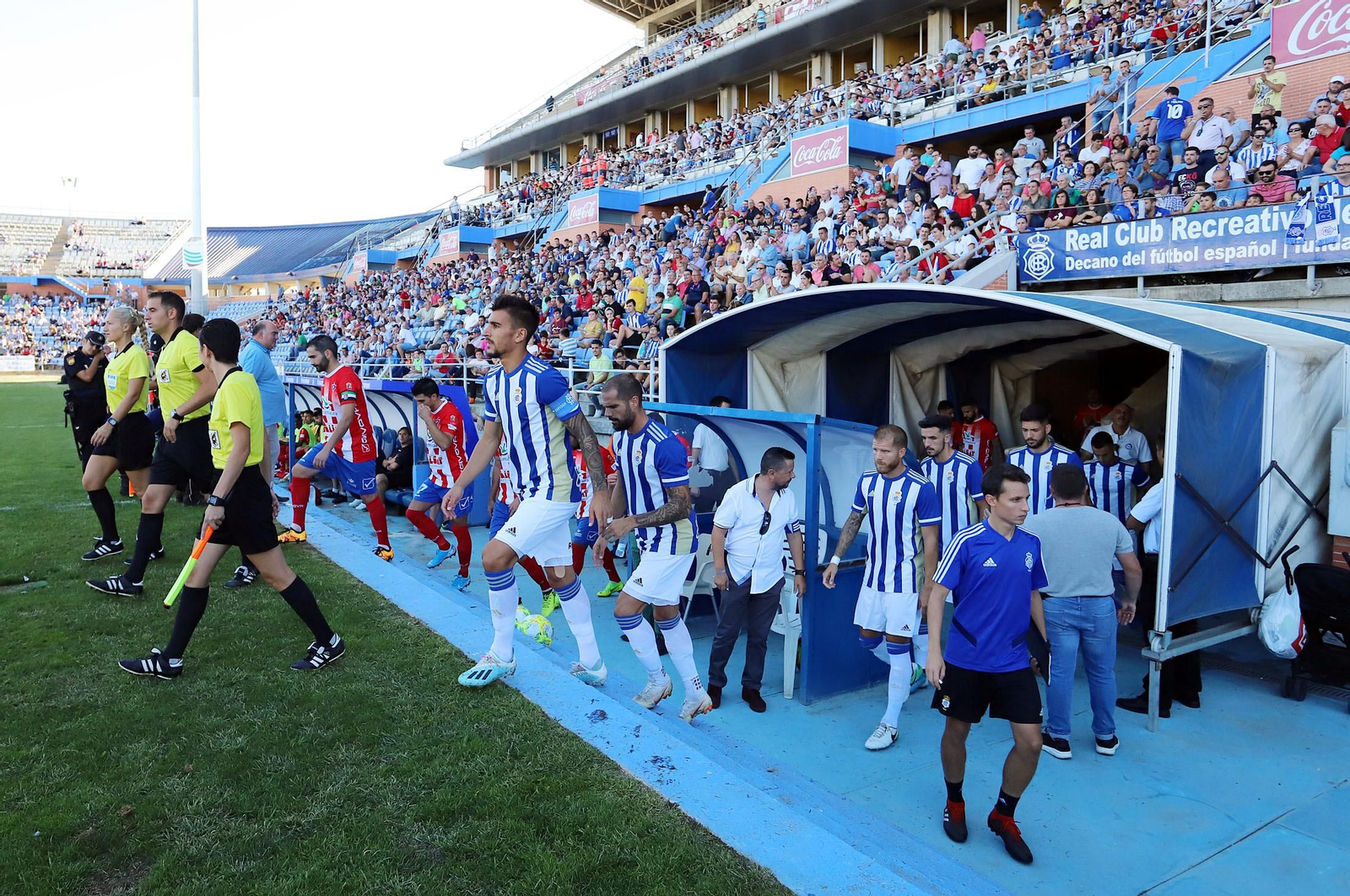 Diego Jiménez sube al césped del Nuevo Colombino desde el túnel de vestuarios tras el trío arbitral, encabezando un once del Recre.