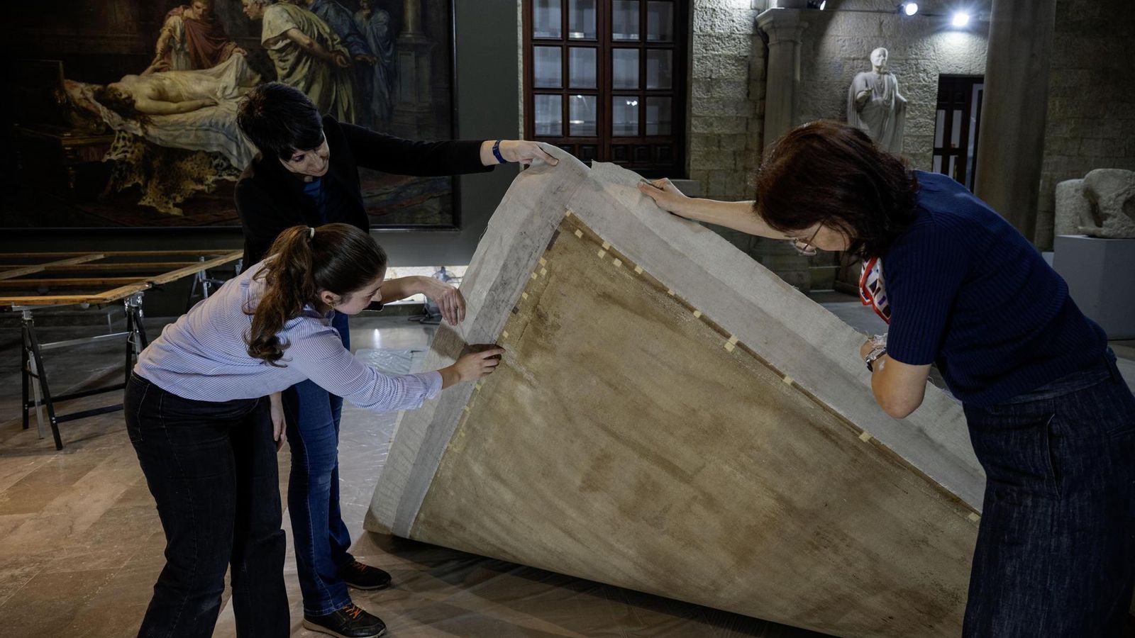 Lucía Martínez Valverde (derecha), restauradora del Museo Nacional del Prado, observa el reverso del cuadro 'Rea Silvia' junto a varias personas del equipo.