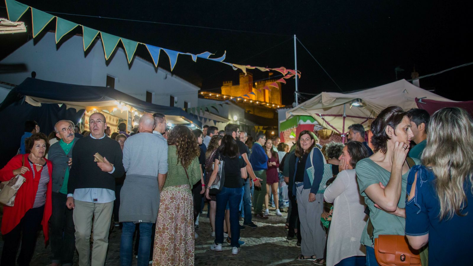 Los visitantes pasean entre los puestos, con el castillo al fondo.