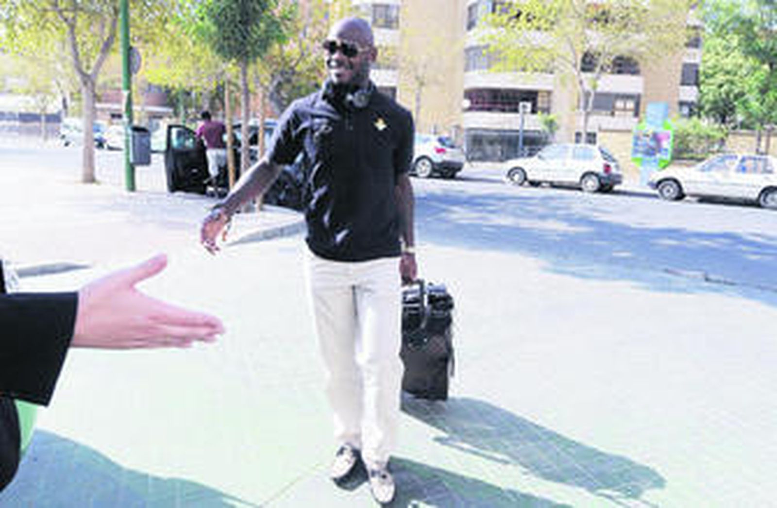 Achille Emana saluda sonriente a un aficionado verdiblanco a su llegada al estadio heliopolitano antes de partir a la estación de Santa Justa para viajar a Madrid en el AVE.