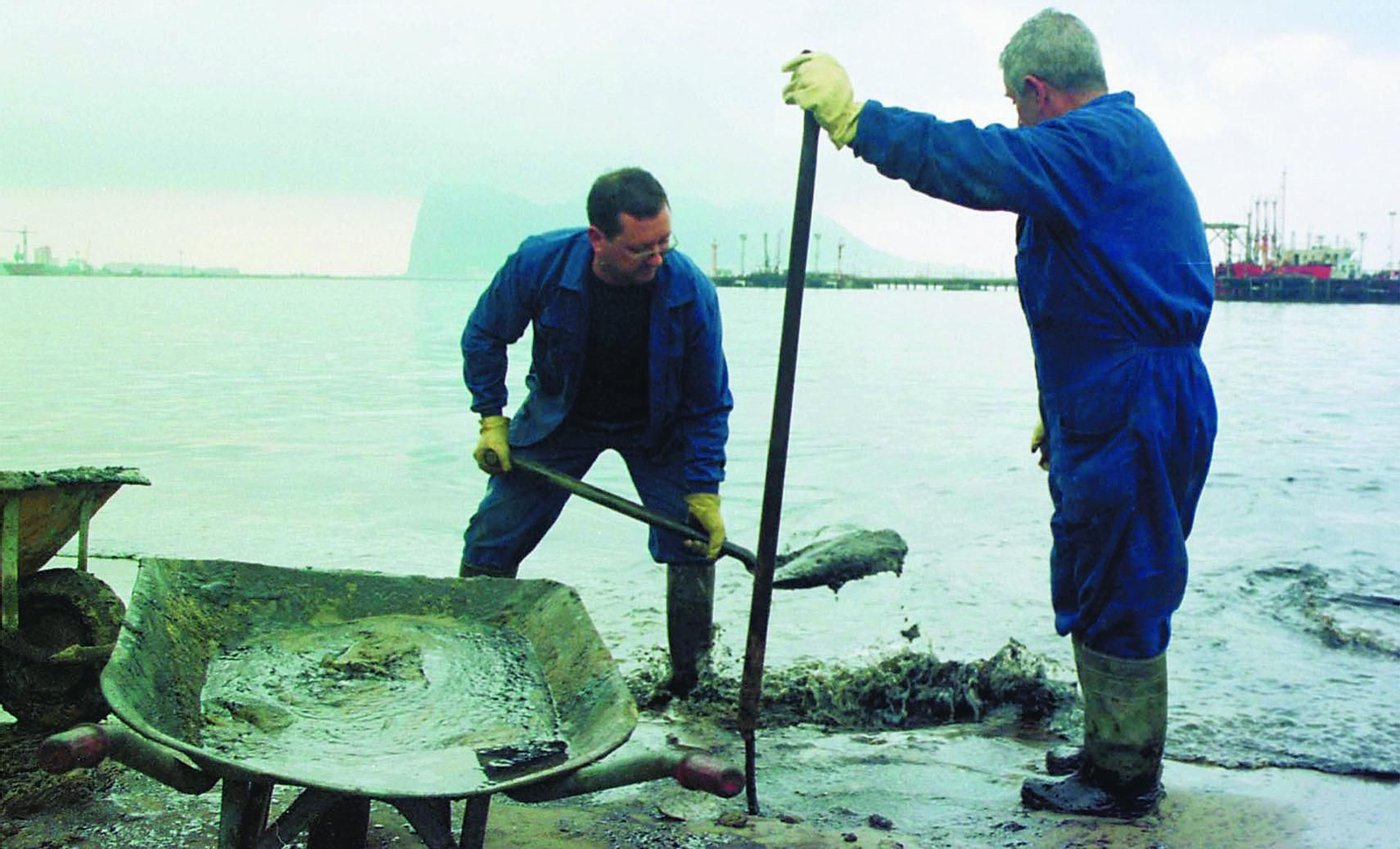 Dos operarios recogen fuel de la playa de Puente Mayorga, el 23 de diciembre de 2002.