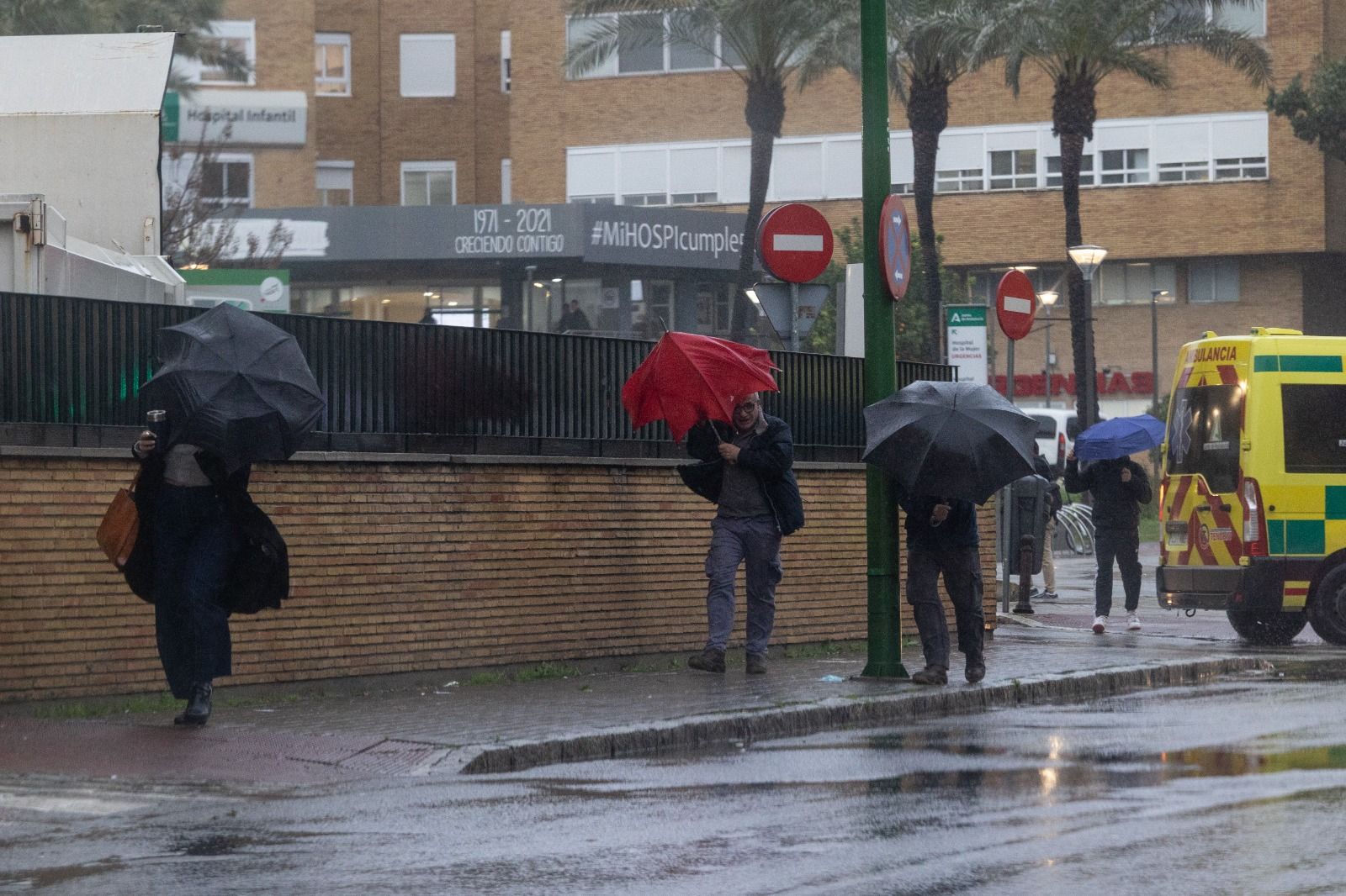 Varios viandantes tratan de protegerse de la lluvia frente al fuerte viento.
