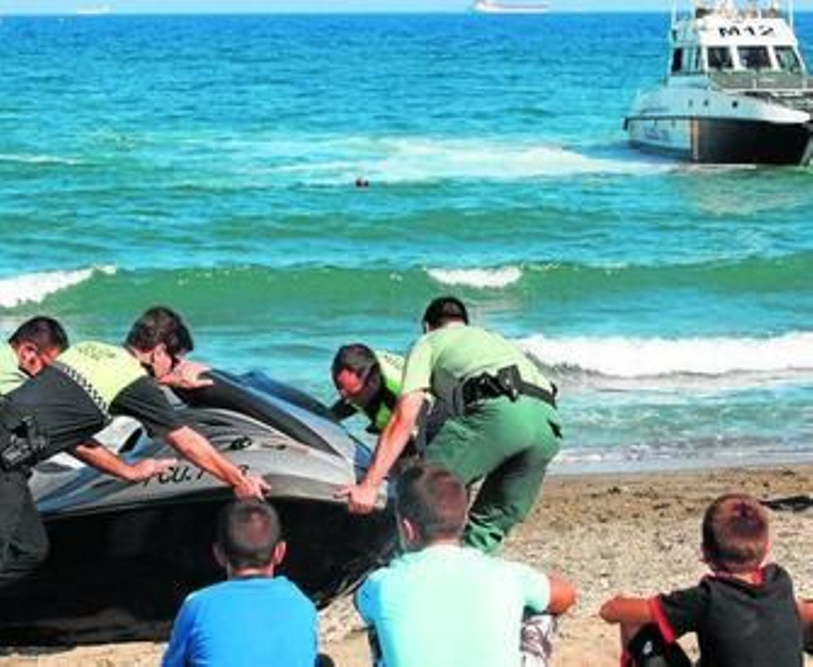 Guardias civiles y policías locales intentan sacar la moto acuática embarrancada en la arena.