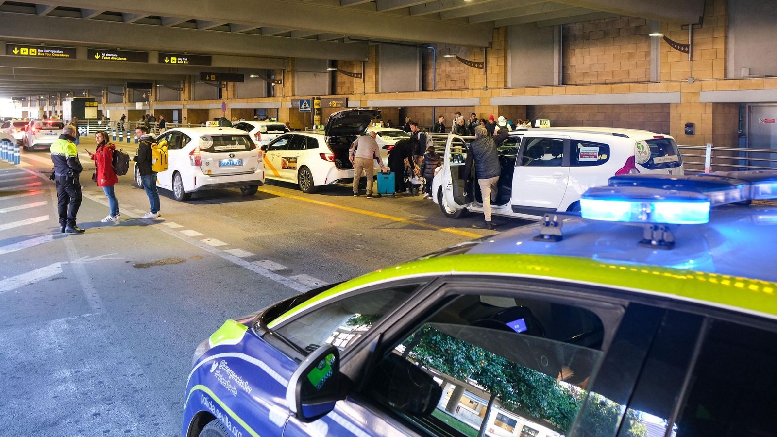 Un policía local atiende a unos pasajeros recién aterrizados en el túnel exterior de Llegadas.