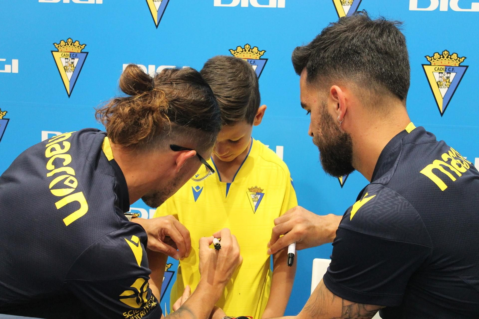 El defensa (i) y el portero estampan su rúbrica en la camiseta de un joven cadista.