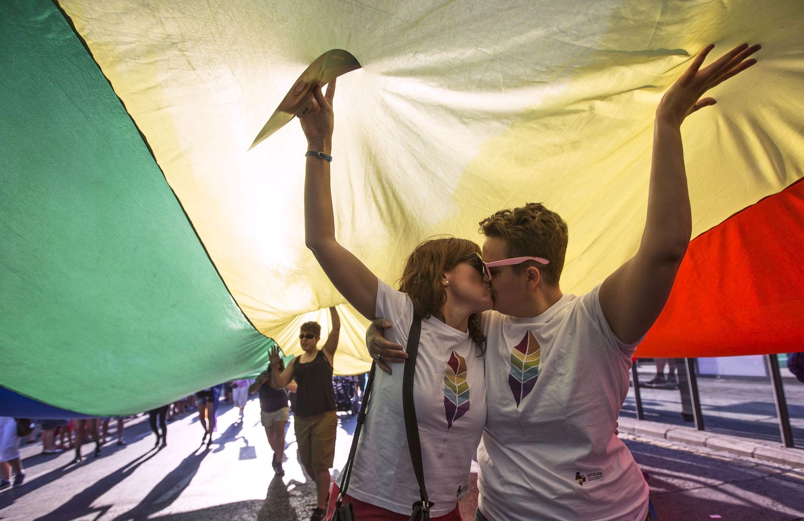 Dos mujeres se besan bajo la bandera arcoiris en una manifestación del Orgullo.