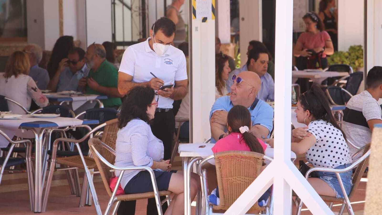 Un camarero atiende a unos clientes en una terraza del paseo marítimo de La Barrosa.