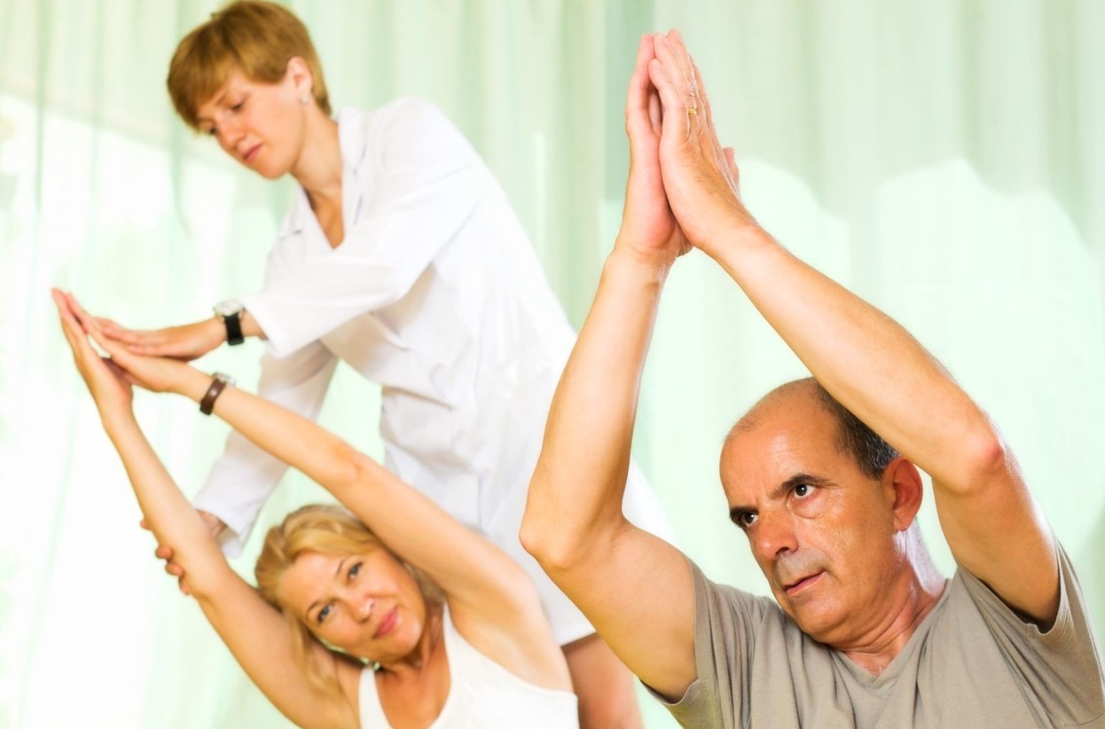 Dos personas mayores practicando actividad física con la ayuda de una profesional