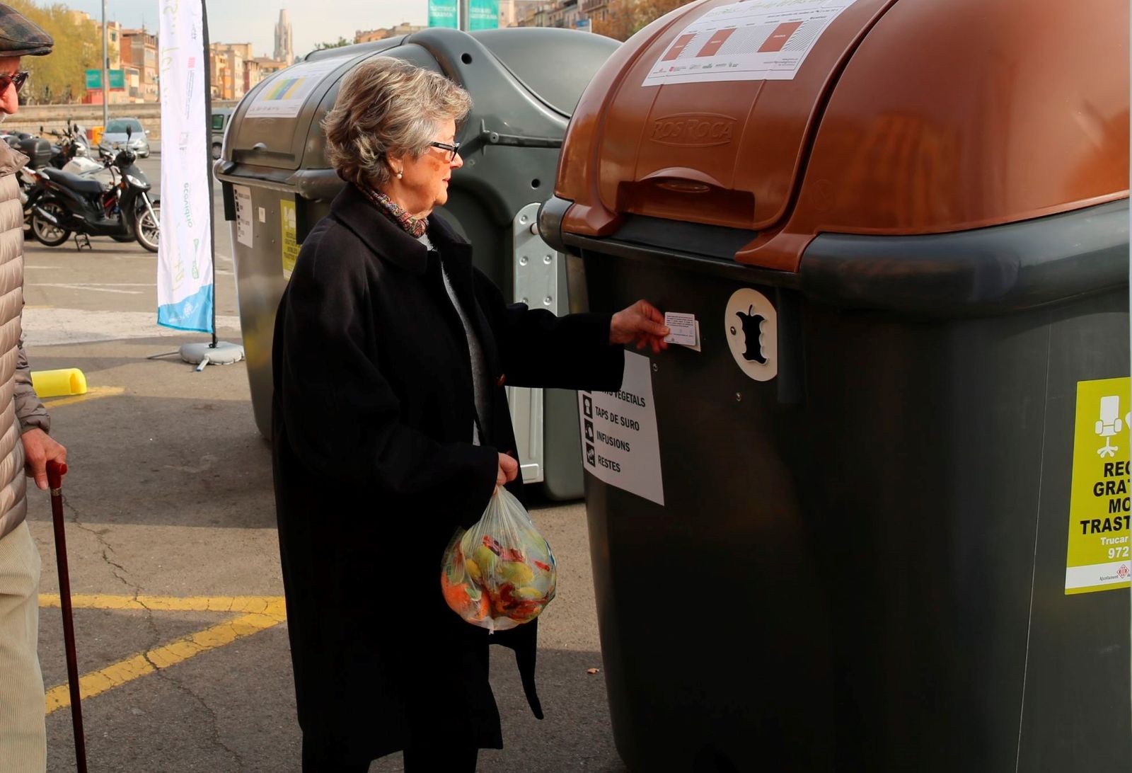 Una mujer deposita residuos orgánicos en un contenedor con tarjeta en Girona.