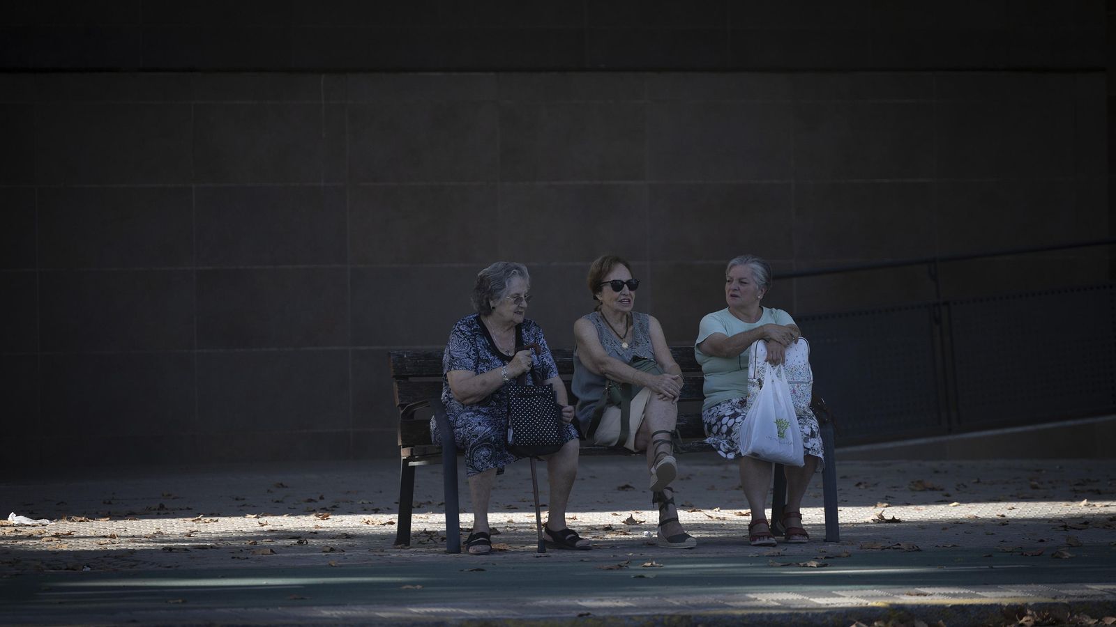 Tres personas mayores sentadas en un banco de la ciudad.
