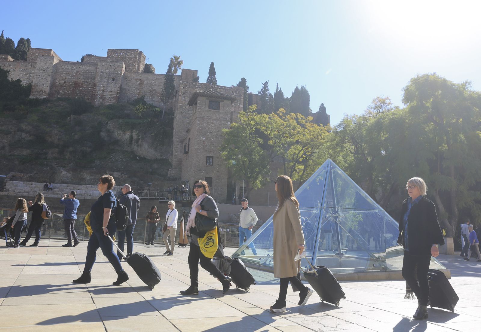 Varias personas llegan a Málaga y pasean junto a la Alcazaba y el Teatro Romano.